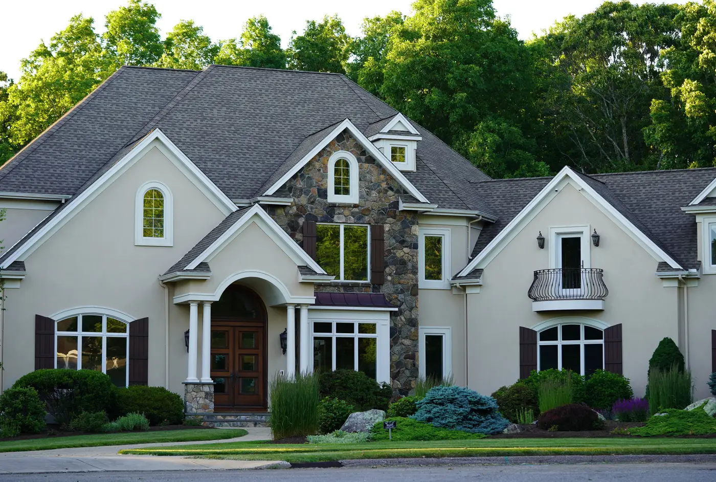 A suburban house with a composition asphalt shingle roof surrounded by trees and greenery.